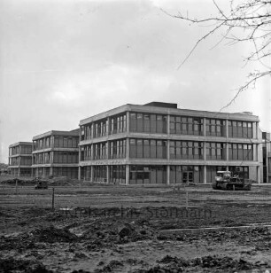 Schulzentrum Glinde: Neubau vor Fertigstellung: hinten drei Gebäudeblöcke vor Fertigstellung: davor unbefestigte Außenanlagen mit Bagger