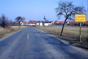 Ortseingangsstraße; Schild, Straße und erste Häuser; Kirchturm