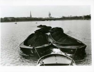 Hamburg. Ein mit Kohle beladener Schleppverband auf der Aussenalster. Im Hintergrund die Kennedy- und Lombardsbrücke und die Silhouette der historischen Innenstadt der Freien- und Hansestadt