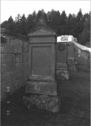 Grabstein 20 (Index: 99609656) Material: Sandstein Zustand: verwittert Maße HxBxT: 205x71x33 cm Beschreibung: Stele, Giebelabschluß mit Verdachung, Mittelpalmette, Schriftfeld rechteckig eingetieft, getreppter Sockel unten Rusticaimitat: Grabstein 20