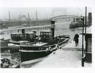 Hamburg. Der Hafen im Winter. Schlepper liegen im vereisten Hafenbecken am Kai. Wo will der Seemann mit seinem Seesack hin?