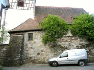 Ansicht von Norden mit Kirche (Kirchturm im Kern Romanisch-Langhaus 1468 erneuert) über Kirchhofmauer (Wehrgang mit Steinbrüstung im 18 Jh abgetragen)