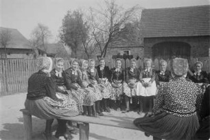 Mädchen in Schleifer Tracht aus Rohne auf der Singebank in Rohne. : Holcy w Slepjanskej drasće z Rowneho na spěwarskej ławcy w Rownom.