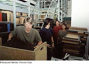 Sächsische Landesbibliothek - Staats- und Universitätsbibliothek Dresden. Zentralbibliothek (ehem. Landesbibliothek). Umzugsvorbereitungen im Magazin-Flachbau (Erdgeschoss). Hilfskräfte laden gestapelte Bestände in einen Bücherwagen : Dresden-Neustadt, Marienallee 12. Sächsische Landesbibliothek - Staats- und Universitätsbibliothek Dresden. Zentralbibliothek (ehem. Landesbibliothek). Umzugsvorbereitungen im Magazin-Flachbau (Erdgeschoss). Hilfskräfte laden gestapelte Bestände in einen Bücherwagen