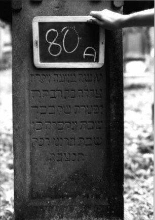 Grabstein 80 (Index: 100090738) Material: Sandstein Zustand: leicht verwittert Maße HxBxT: 156x50x21 cm Beschreibung: getreppt. Sockel, giebelart. Abschl. m. Verdach. , Schriftfeld mit Rundbogen Symbolik: gestelztes giebelartiges Rundbogenfries: Grabstein 80A