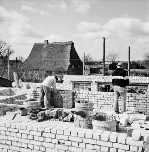 Baustelle eines Wohngebäudes, dahinter ein Reetdachhaus