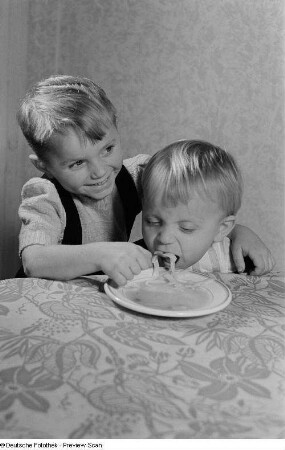 Ein Kind beim Füttern eines Jüngeren mit Nudelsuppe