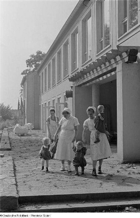 Pflegerinnen mit Kindern vor dem Heimgebäude