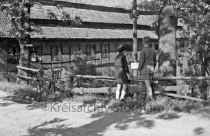 Drahtmühle: vorn Weg: rechts zwei Jungen auf Holzgeländer: dahinter Bäume und Warnschild an Mast