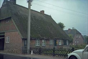 Havighorst: Dorfstraße 18: Bauernhaus mit Reetdach: Traufseite mit Eingangstür: links giebelständige Straßenseite Wirtschaftstrakt mit Scheunentor
