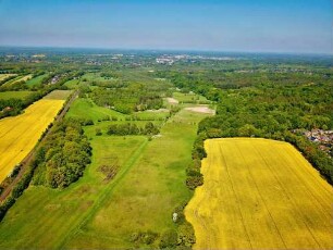 Ahrensburg: Luftbild des Ortsteils Am Hagen in Blickrichtung Norden: links und rechts blühende Rapsfelder, mittig Bahnstrecke Richtung Ahrensburg, im Hintergrund Stellmoor-Ahrensburger Tunneltal