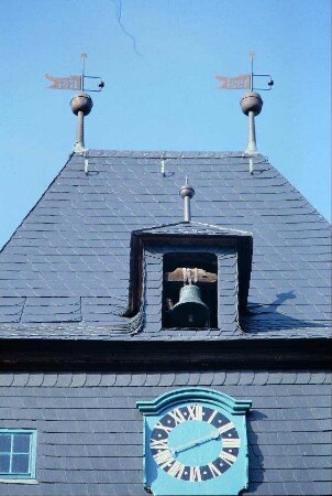 Kirchturmspitze mit 2 Wetterfahnen, kleine Glocke in Mansarde, darunter Uhr