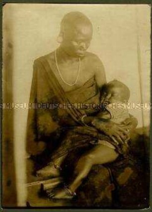 Sitzende Massai-Frau mit Kleinkind auf ihrem Schoß