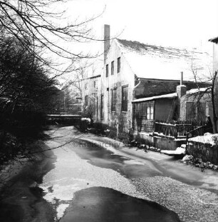 Trave: Stadtarm hinter Hindenburgstraße mit Eisdecke: links Sträucher und Bäume: rechts Gebäude: hinten links Fußgängerbrücke: Winter