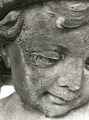 Putto mit Päckchen und Geldbeutel. Um 1905. Sandstein. Figur auf dem Ständehaus, Detail Gesicht während der Substanzsicherung/Wiederaufbau Dach. Dresden-Altstadt, Schloßplatz 1