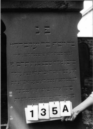 Grabstein 135 (Index: 100094249) Material: Sandstein Zustand: verwittert im Giebel Maße HxBxT: 190x64x29 cm Beschreibung: kon. Stele, profiliert. Sockel, eingezogener GIebel mit Mittelakroter Symbolik: Blätter im Akroter Besonderheit: gereimter 4-Zeiler: Grabstein 135A
