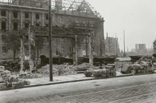 Blick über Gebäudereste, gestapelte Steine und Gleisanlagen der "Trümmerbahn" mit Muldenkipploren gegen Neues Rathaus