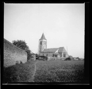 Carnin (Dep. Nord, Frankreich): "Kirche von Carnin", im Vordergrund ein Feld und eine Grundstücksmauer (Distanzaufnahme)