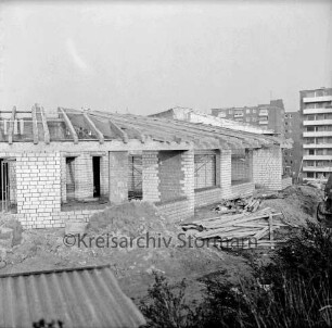 Evangelisches Gemeindehaus: Masurenweg: Rohbau: davor Erdhaufen, Bretterhaufen, Baumaterial, Gestrüpp: hinten rechts Hochhäuser