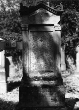 Grabstein 64 (Index: 100086519) Material: Sandstein Zustand: Schrifttafel fehlt Maße HxBxT: 174x59x23 cm Beschreibung: ädikulaartige Stele mit Pilastern, getreppter Sockel, eingezogener giebelartiger Abschluß mit Verdachung und Akroteren Symbolik: achtzackiger Stern: Grabstein 64