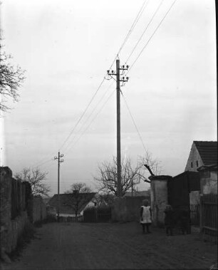 Sachsen? Erste 110 kV-Freileitung des Elektroarmaturenwerks Radebeul-Kötzschenbroda. Dorfstraße mit Leitungsmasten. Blick gegen Gehöfte