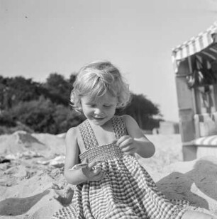 Kleines Mädchen mit Sonnebrille sitzt am Strand von Henkenhagen (heute: Ustronie Morskie)