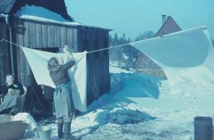 Erzgebirge. Verschneite Wohnhäuser, Frau beim Aufhängen von Wäsche