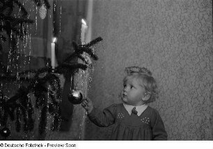 Porträt eines kleinen Mädchens mit Christbaumkugel an einem Weihnachtsbaum
