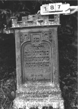 Grabstein 187 (Index: 100106285) Material: Sandstein Zustand: leicht verwittert, teilweise abgeblättert, teilweise Textverlust, Mittelaufsatz fehlt Maße HxBxT: 130x66x19 cm Beschreibung: Stele mit Walmdach und Zinnenvorsatz, Mittelaufsatz fehlt, Schriftfeld eingetieft mit Schulterbogenabschluß, getreppter Sockel Symbolik: floral: Grabstein 187