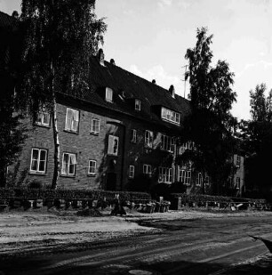 Hebbelstraße: Ausbau: vorn unbefestigte Straße, Stapel mit Gehwegplatten und Mülleimer: dahinter Wohnhäuser der Gemeinnützigen Baugenossenschaft Bad Oldesloe mit Vorgärten