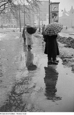 Menschen mit Regenschirmen warten an der Straßenbahnhaltestelle auf dem Martin-Luther-Ring, im Hintergrund das Reichsgericht