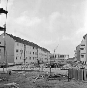 Klosterbergen: Bogenstraße: rechts und links dreigeschossige Wohnblocks vor Fertigstellung: vorn und in der Mitte Reste von Baumaterial auf unbefestigtem Gelände: links Baugerüst: in der Mitte Pkw und Fahrrad: links dahinter Lieferwagen mit zwei Personen vor Eingang: hinten Mitte achtgeschossiges Punkthaus im Bau: davor Baukran