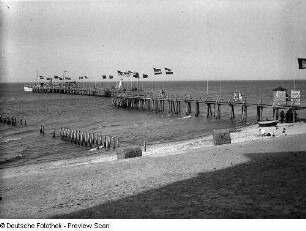 Blick über den Ostseestrand zur Seebrücke mit Flaggen