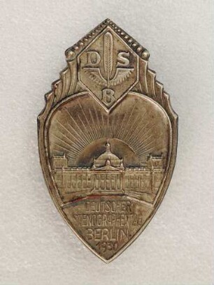 Ereignisabzeichen Deutscher Stenographentag Berlin 1930 (mit Broschennadel) : Medaillensammlung Stenografische Sammlung. Ereignisabzeichen Deutscher Stenographentag Berlin 1930 (Wappenschild mit Reichstagsgebäude vor Sonnenaufgang, darüber Emblem des Deutschen Stenografenbundes, darunter Gravurtafel "Deutscher Stenographentag Berlin 1930", mit Broschennadel; rückseitig: Rob. Neff W. 30 Berlin). Metall; Maße 47 x 27 mm (1930; Rob. Neff, Berlin). Dresden: SLUB R c 0472