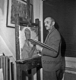 Rudolf Greve: Maler: in Atelier: vor Staffelei mit Gemälde: in Hand Pinsel und Palette