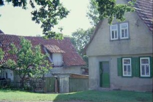 Giebel eines einstöckigen, kleinen Hauses; dahinter Wirtschaftsgebäude