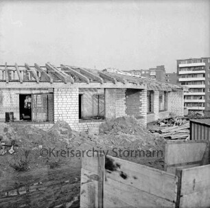 Evangelisches Gemeindehaus: Masurenweg: Rohbau: davor Erdhaufen, Bretterstapel, Baumaterial: vorn rechts Bretterverschlag: hinten rechts Hochhäuser