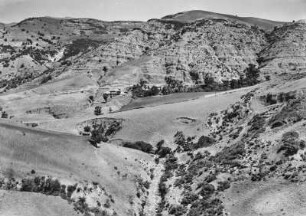 Landschaft : Blick über die von Erosionsrissen zerklüftete Landschaft, an den Hängen Weizen, Weiden und Macchie.