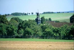 Feld, Wiese, Staketenzaun, Gärten mit Obstbäumen; der Kirchturm ragt heraus