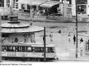 Dresden-Altstadt. Postplatz. Blick über die Straßenbahnhaltestelle mit Wartehäuschen (sogenannte Käseglocke) gegen Lebensmittelladen