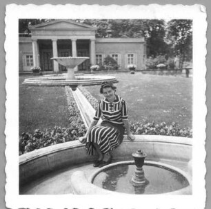Frau, auf dem Rand eines Brunnenbeckens in einem Park sitzend