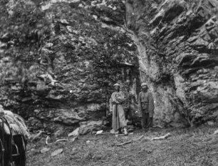 Doppelportrait : Portrait zweier Männer aus Zentralasien, möglicherweise Expeditionsmitglieder, vor einer Felswand im Tian Shan Hochgebirge