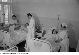 Blick in ein Krankenzimmer mit Arzt, Krankenschwestern und Patienten