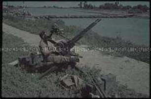 Soldat an einer Flugabwehrkanone am Ufer eines Flusses