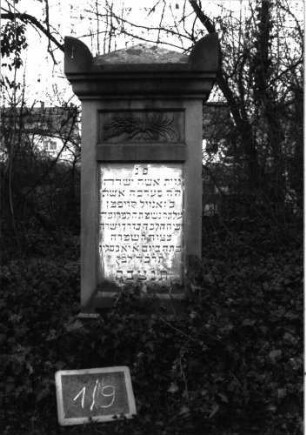 Grabstein 9 (Index: 99804885) Material: Sandstein Zustand: Sockel verwittert Maße HxBxT: 149x61x25 cm Beschreibung: Stele, Sockel, Giebel mit Eckakroteren, eingetieftes Schriftfeld rechteckig Symbolik: gebundene Blätterwedel: Grabstein 1/9
