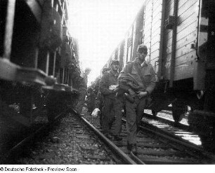 Deutschland . Truppenübungsplatz Klietz. Nationale Volksarmee - Landstreitkräfte. Truppenverlegung per Eisenbahnmarsch. Soldaten zwischen zwei Militärzügen (links Flachwagen mit Militärtechnik, rechts Mannschaftswagen)