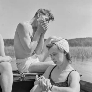 Elisabeth Gremmler (links) und ein befreundeter Mann sitzen auf einem Segelboot, er spielt Mundharmonika