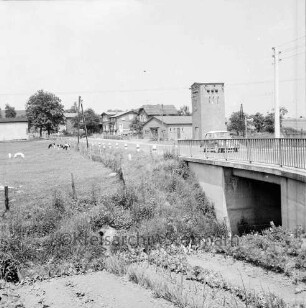 Brücke über Heilsau mit Pkw: vorn Garten: hinten links Weiden mit Schweinen und Rindern: rechts Umspannstation: im Hintergrund Bauernhäuser und Bäume