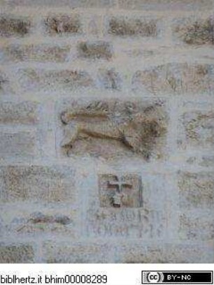 Zwei vermauerte Reliefs: Löwe (Teil von Wappen Precis?) und kreuzhaltende Hand mit gotischer Inschrift