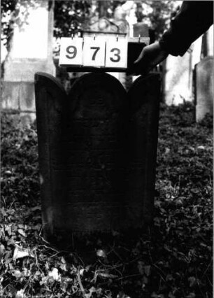 Grabstein 973 (Index: 99804018) Material: Sandstein Zustand: leicht verwittert Maße HxBxT: 73x45x11 cm Beschreibung: Stele mit eingezogenem Rundbogen, Seitenakroterien, profilierter Rand Besonderheit: Endreim: Grabstein 973